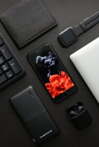 Top-down view featuring gadgets like a smartphone, smartwatch, and wireless earbuds on a black surface.